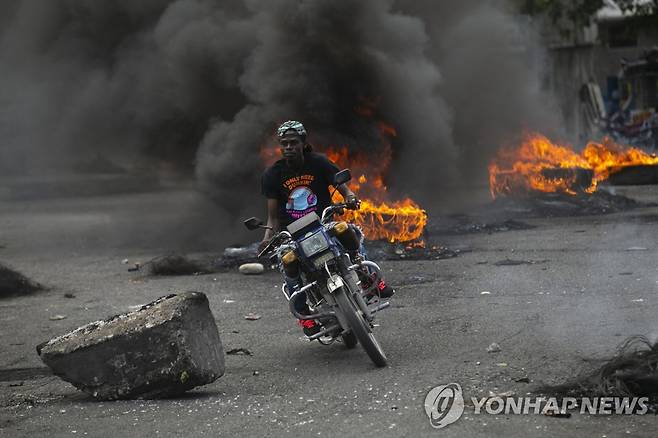 아이티 포르토프랭스에서 붙 타는 장애물을 뒤로 한 채 오토바이를 운전하는 시민 [AP 연합뉴스 자료사진. 재판매 및 DB 금지]