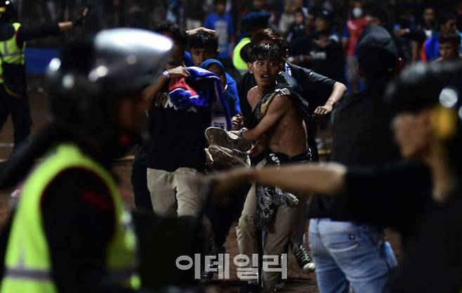 인도네시아 동부 자바주 말랑 리젠시 칸주루한 축구장에서 폭동 사태가 벌어진 가운데 한 남성이 쓰러진 남성을 안고 달리고 있다./ 사진=게티이미지