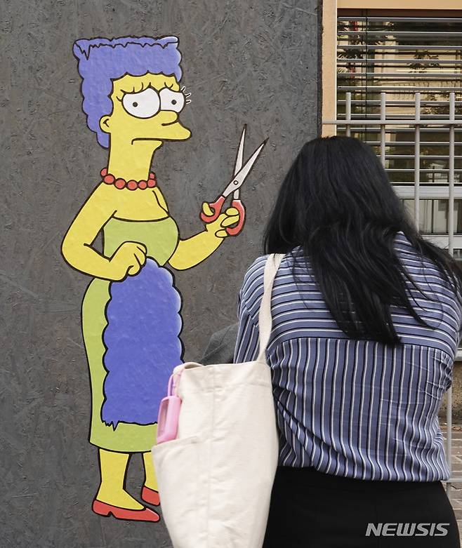[밀라노=AP/뉴시스] 5일(현지시간) 이탈리아 밀라노에 있는 이란 영사관 앞에서 한 여성이 '심슨 가족'의 로지 심슨이 가위를 들고 자신의 머리카락을 자른 '커트'라는 제목의 벽화를 사진 찍고 있다. 2022.10.06.