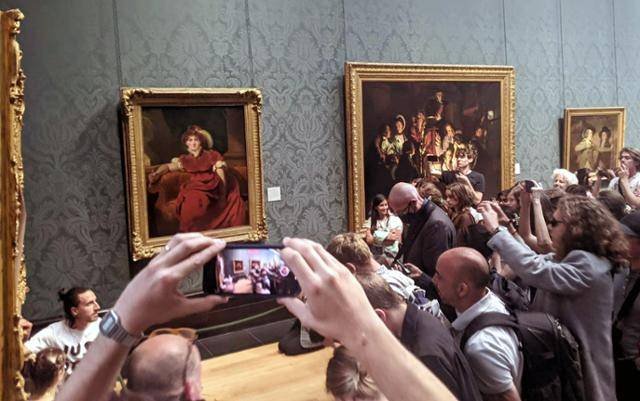 저스트 스톱 오일 소속 회원들이 7월 5일 영국 런던의 국립미술관에서 존 커스터블의 작품인 '건초 마차'에 접착제 바른 손을 붙인 채 시위를 벌이자 관객들이 몰려 사진을 찍고 있다. 페이스북 캡처