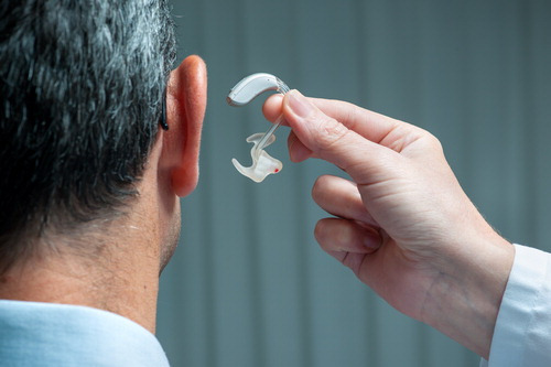 Doctor inserting, hearing aid in senior's ear