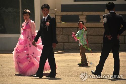 북한의 결혼식 풍경     (서울=연합뉴스) 연합뉴스가 2016년 6월 14일 입수한 북한 사진에 지인들의 축복을 받으며 결혼하는 젊은 신랑, 신부의 모습이 포착됐다. 또 중국산 '나이키' 운동화를 신고 부부를 쫓아가는 어린이의 모습도 함께 나타났다. 사진은 가족과 지인의 축복을 받는 부부의 모습. 2022.11.12
    << 국내에서만 사용가능. 재배포 금지. For Use Only in the Republic of Korea. No Redistribution >>