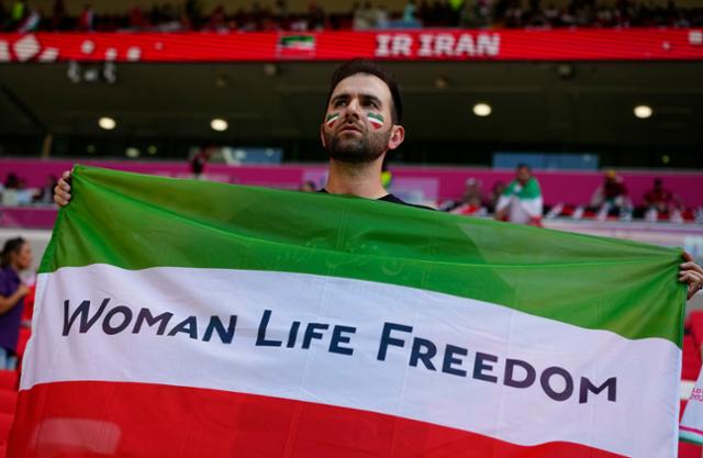 지난 25일 열린 카타르 월드컵 조별리그 B조 이란과 웨일스와의 경기 전 한 이란인 팬이 국기 중간에 '이슬람공화국 문양' 대신 '여성, 삶, 자유'라고 쓴 깃발을 들고 반정부 시위 지지 의사를 밝히고 있다. 알라얀=AP