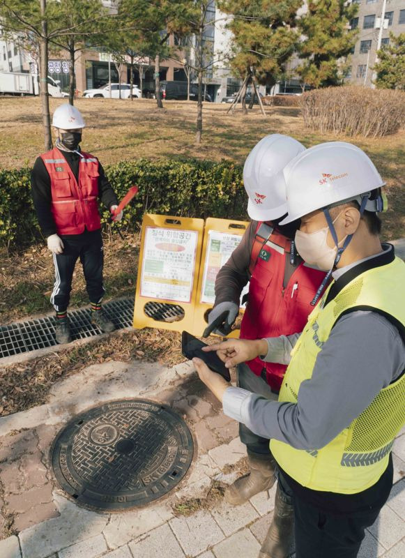 SK텔레콤과 SK오앤에스 작업자들이 IoT 센서로 측정한 맨홀 내부 정보를 스마트폰으로 확인하고 작업을 진행하고 있다. SKT 제공