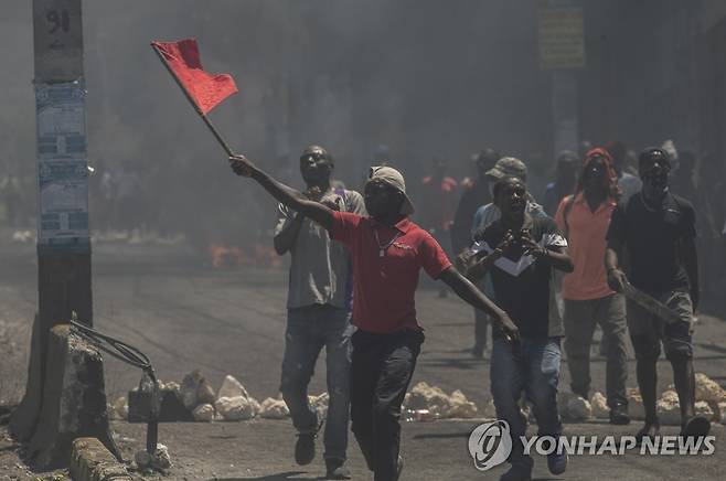 적색기 흔들며 시위하는 아이티 남성 (포르토프랭스 AP=연합뉴스) 15일(현지시간) 아이티 수도 포르토프랭스 시내에서 연료 가격 인상 등에 항의하며 아리엘 앙리 총리의 퇴진을 촉구하는 시위대 속 한 남성이 적색 깃발을 흔들고 있다. 아이티에서는 활보하는 폭력조직에 더해 극심한 연료난에 성난 주민 시위가 이어지면서 사회 불안이 가중되고 있다. 2022.9.16 leekm@yna.co.kr