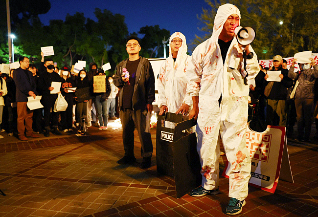 11월 29일 미국 캘리포니아주 서던캘리포니아대(USC) 로스앤젤레스에서 열린 중국 우루무치 화재 사고 희생자들을 기리는 촛불집회에서 한 시위자가 중국 방역요원을 조롱하는 의미에서 흰색 방호복을 착용한 채 확성기를 통해 반중 구호를 외치고 있다.   AFP 연합뉴스