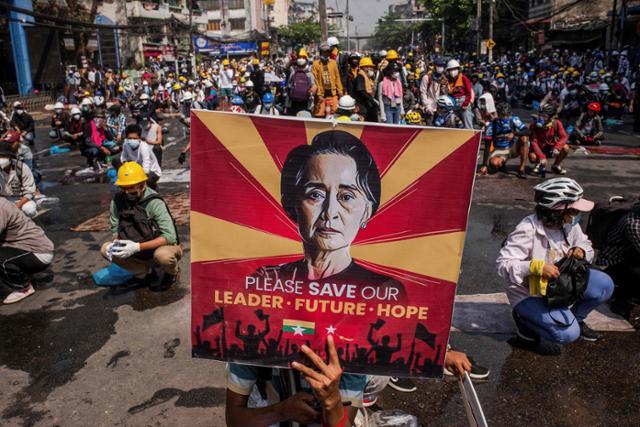 지난해 3월 미얀마 양곤에서 군부 쿠데타를 반대하는 시민들이 가택 연금 중인 아웅산 수치 국가고문 얼굴이 그려진 포스터를 들고 시위하고 있다. 양곤=AFP 연합뉴스