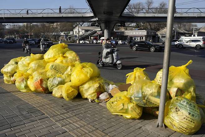 [베이징=AP/뉴시스] 7일 중국 베이징에서 주민들이 의료폐기물이라고 표시된 노란색 쓰레기봉투가 쌓인 거리를 지나가고 있다. 중국 국무원이 코로나19 규제 완화책으로 10개 조치를 발표하면서 앞으로 고위험 지역이 아니면 지역 간 이동에 제한받지 않고 무증상 감염자와 경증 환자는 원칙적으로 자가격리가 허용되는 등 '제로 코로나'가 '위드 코로나'로 바뀔 것으로 기대되고 있다. 2022.12.07.