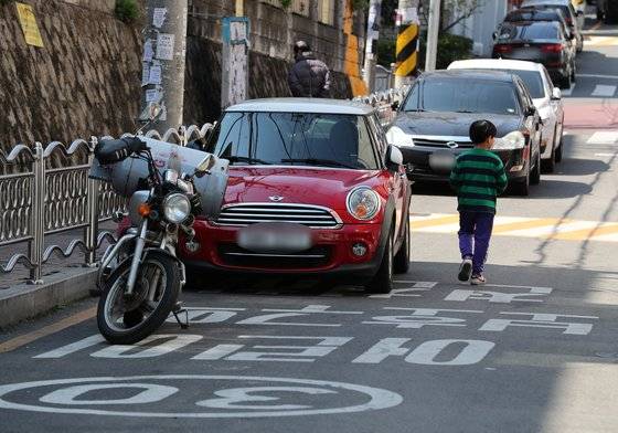 민식이법 시행 첫날인 2020년 3월 25일 부산 동래구 한 초등학교에 불법 주차된 차량 옆으로 한 어린이가 보행 하고 있다. 연합뉴스