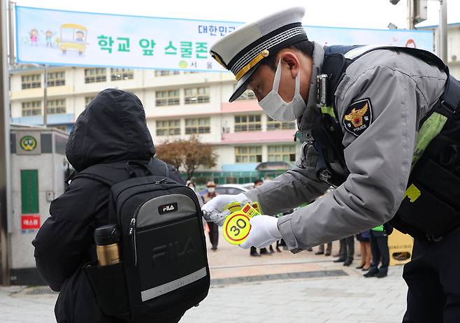 지난달 22일 열린 ‘안전한 등굣길 교통안전 캠페인’에서 경찰이 스쿨존 내 안전 속도인 시속 30km를 의미하는 숫자 ‘30’이 적힌 열쇠고리를 학생의 가방에 달아주고 있다. 연합뉴스