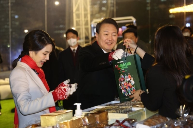 윤석열 대통령(가운데)과 부인 김건희 여사(왼쪽)가 지난 16일 서울 종로구 송현광장에서 열린 윈·윈터 페스티벌 개막식에 참석, 에어돔 부스에서 물건을 사고 있다. 대통령실통신사진기자단. 연합뉴스