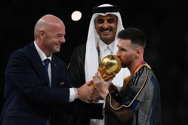 TOPSHOT - Argentina's forward #10 Lionel Messi kisses the World Cup trophy as FIFA President Gianni Infantino and Qatar's Emir Sheikh Tamim bin Hamad al-Thani look on during the Qatar 2022 World Cup trophy ceremony after the football final match between Argentina and France at Lusail Stadium in Lusail, north of Doha on December 18, 2022. - Argentina won in the penalty shoot-out. (Photo by FRANCK FIFE / AFP)<저작권자(c) 연합뉴스, 무단 전재-재배포 금지>