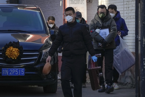 중국 베이징의 한 발열 진료소 앞에서 지난 19일 영정 사진을 든 유족들이 시신을 운반하는 영구차 옆으로 지나가고 있다. AP연합뉴스