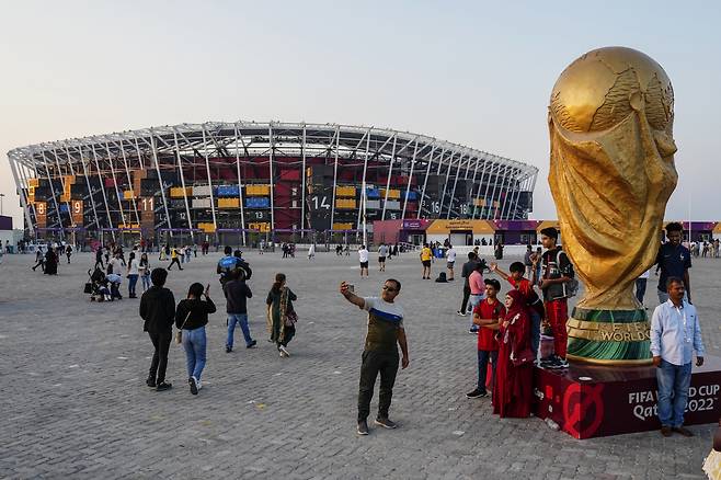 People pose for pictures next to a replica of the World Cup Trophy, right, with the Stadium 974 in the background before the Qatar Fashion United event in Doha, Qatar, Friday, Dec. 16, 2022. (AP Photo/Pavel Golovkin)<저작권자(c) 연합뉴스, 무단 전재-재배포 금지>