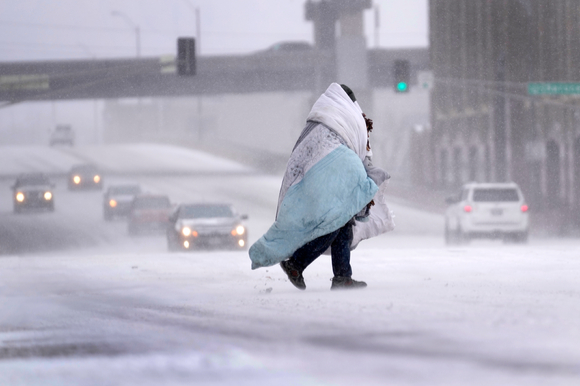 22일(현지시간) 미 미주리주 세인트루이스에서 담요로 몸을 에워싼 노숙인이 눈 내리는 도로를 건너고 있다. 성탄절을 앞두고 미국 대부분 지역에 혹한과 거센 겨울 폭풍, 눈보라가 엄습하는 악천후가 이어지면서 미국인들의 연휴 여행 계획에 차질을 빚고 있다. [사진=뉴시스]