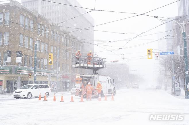 [토론토=AP/뉴시스]23일(현지시간) 캐나다 토론토에서 눈보라가 치는 동안 작업자들이 강풍으로 손상된 전선을 수리하고 있다. 2022.12.24.