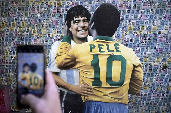 A man takes a picture of a wall depicting an image of late football stars Diego Maradona of Argentina and Pele of Brazil embracing each other, in Buenos Aires on December 29, 2022, just hours after the passing of Pele. (Photo by Juan MABROMATA / AFP)

<저작권자(c) 연합뉴스, 무단 전재-재배포 금지>