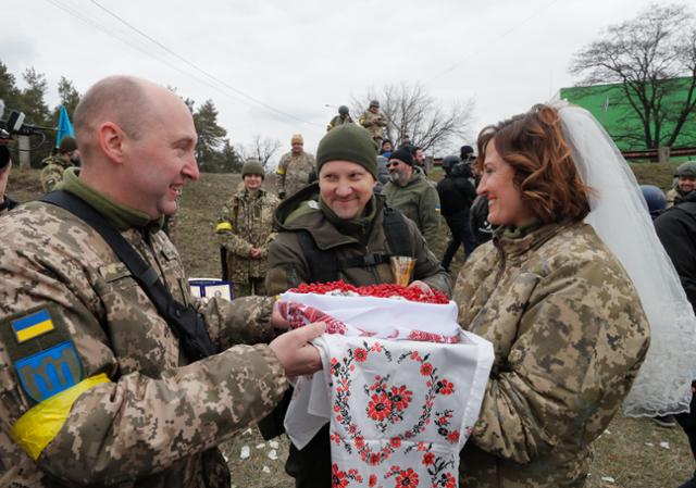 지난해 3월 6일 우크라이나 키이우 인근 블록포스트에서 방위군 대원인 발레리(가운데)와 레샤(오른쪽)가 결혼식을 하고 있다. 블록포스트=EPA 연합뉴스