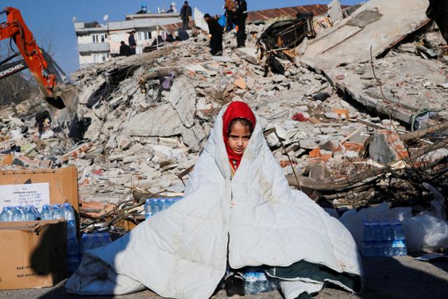 지진으로 붕괴된 튀르키예 카라만마라슈의 집터에서 한 소녀가 이불을 뒤집어 쓴 채 가족을 기다리고 있다. 카라만마라슈(튀르키예)=로이터 연합뉴스
