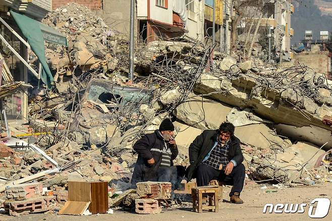규모 7.8 지진 발생 나흘째인 9일(현지시간) 튀르키예 아디야만에서 사망자 유가족들이 무너진 건물 잔해 옆에 앉아 담배를 피우고 있다. 2023.2.9. ⓒ AFP=뉴스1 ⓒ News1 김성식 기자