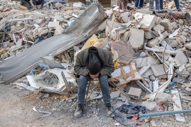 12일(현지시각) 튀르키예 하타이에서 남성 한명이 구조 작업이 진행되고 있는 건물 잔해 앞에 앉아 얼굴을 파묻고 있다. 하타이/AFP 연합뉴스