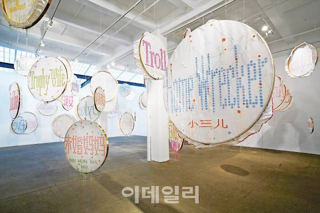린톈먀오의 ‘배지’(Badge·2011∼2012). 설치미술가이자 섬유디자이너로 활약하는 린톈먀오가 두 타이틀을 한자리에 응축한 대표작. 실과 자수란 소재·기법으로 거대한 설치작품을 만들었다. 사전어는 물론, 비속어·신조어까지 포함해 ‘여성’을 뜻하는 수많은 단어를 영어·중국어로 수놓은 자수틀 수십 개를 천장에 매달았다. 2012년 미국 뉴욕 갤러리르롱에서 전시(10. 25∼12. 15)했을 때의 전경이다. 비단·실·자수틀·음향, 61피스(각 지름 55㎝, 80㎝, 100㎝, 120㎝), ⓒ린톈먀오·갤러리르롱 제공(ⓒLin Tianmiao, Courtesy Galerie Lelong & Co.).