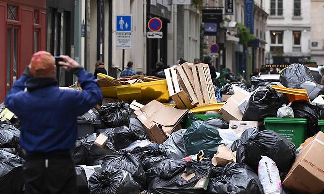 지난 12일(현지시간) 프랑스 파리에서 한 시민이 수거되지 않은 채 거리에 쌓인 쓰레기 더미의 사진을 찍고 있다. 프랑스에서는 연금 개혁에 맞서 노조 파업이 이어지고 있다. 파리=AFP연합뉴스