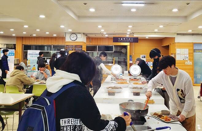 학생들이 자율배식코너에서 식판에 음식을 담고 있다.