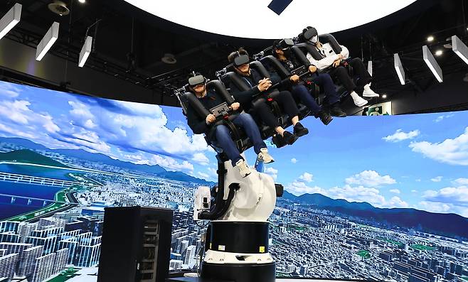 SK텔레콤 부스에서 관람객이 대형 로봇팔에 탑승해 도심항공모빌리티(UAM) 운항 체험을 하고 있다.
