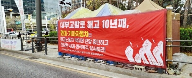 < ‘흉물 현수막’ 덕지덕지 > 기아 판매 대리점 대표와의 갈등 등으로 용역계약이 해지된 A씨는 고용 관계가 없는 기아에 ‘원직 복직’을 요구하며 10년째 농성 중이다. 10일 오전 서울 양재동 현대차그룹 본사 앞 보행도로에 A씨가 설치한 불법 천막, 현수막 등이 방치돼 있다. 김일규 기자