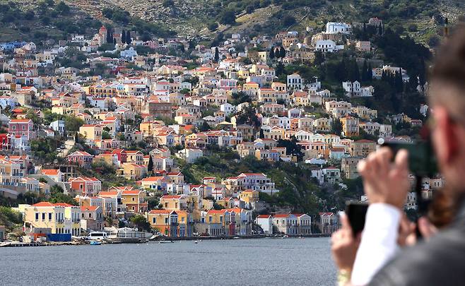 배를 타고 지중해를 건너 온 사람들이 시미섬에 도착하자 시미섬 항구 주변으로 집들이 모여있는 광경을 카메라에 담고 있다. / 오종찬 기자