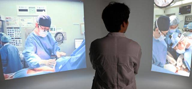 지난달 28일 한국일보를 찾은 수도권 대학병원 수술실 PA 간호사 김정환(39·가명)씨가 과거 자신이 했던 수술 장면 사진을 바라보고 있다. PA 업무는 불법인 탓에 신분을 드러내는 게 쉽지 않다. 카메라를 등지고 선 김씨가 입고 있는 흰 의사 가운은 PA 간호사 시절 병원에서 실제 착용했던 유니폼이다. 홍인기 기자