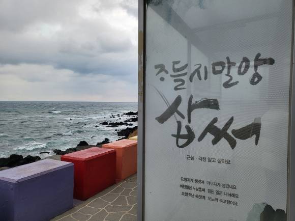 도두동 무지개다리 인근 정류장에 있는 제주도 사투리 ‘조들지말앙 삽써’(근심걱정말고 살아요)홍보 간판. 제주 강동삼 기자