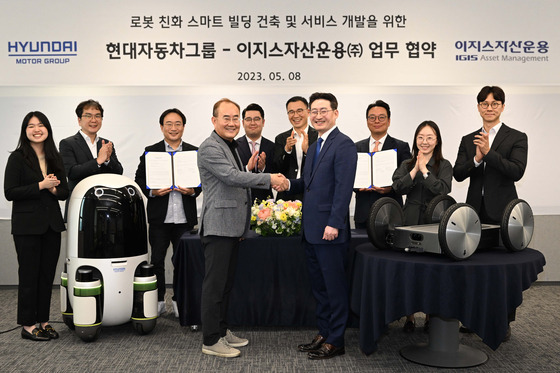 Hyundai Motor and Kia Vice President Kim Yong-wha, left in the front row, and Jung Sock-woo, head of IGIS Asset Management's real asset department, take a photo with MobED, the company's delivery, robot Tuesday. [HYUNDAI MOTOR]