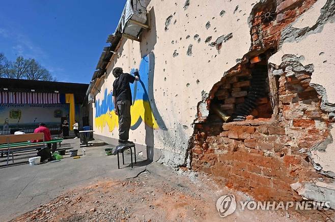 우크라이나 하르키우 지역의 파손된 벽에서 한 예술가가 우크라이나 국기 그림을 그리고 있다.[AFP=연합뉴스]
※ 기사 내용과 직접 관련이 없음