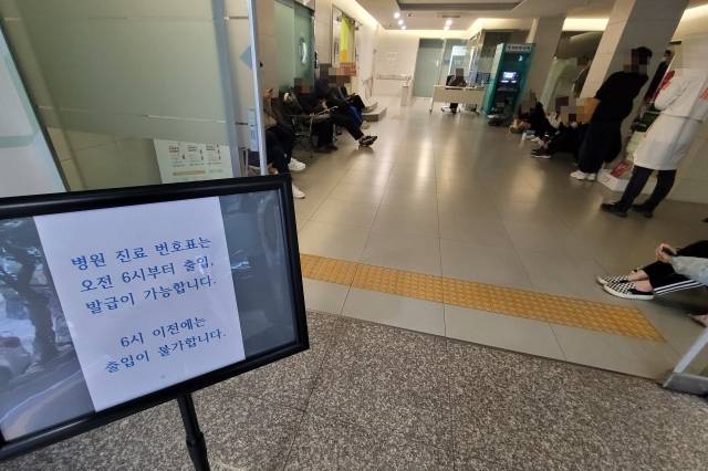 병원 입구에 '번호표는 오전 6시부터 출입, 발급이 가능합니다'라고 적힌 문구가 보인다. 건물 내부에 번호표를 뽑기 위해 기다리고 있는 사람들이 있다. 김판 기자