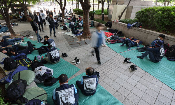 지난 17일 출근시간대 시민들이 서울 중구 청계광장에서 전날 밤 총파업 결의대회 후 노숙하고 있는 민주노총 건설노조원들을 지나치고 있다. 연합뉴스