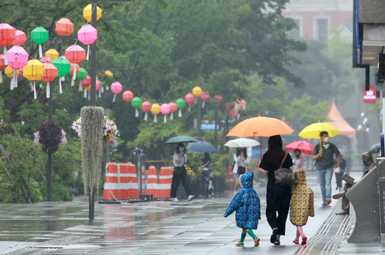 A mother covers her two children with an umbrella in Gwanghwamun Square, central Seoul on Sunday. [YONHAP]