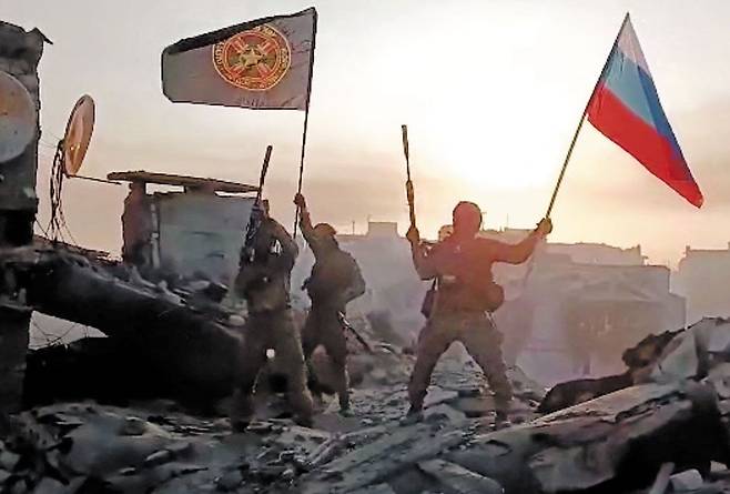 러시아 용병대인 와그너그룹 병사들이 우크라이나 전쟁으로 포격된 것으로 보이는 한 건물 꼭대기에서 와그너그룹 깃발과 러시아 국기를 흔들고 있다. 와그너그룹은 20일(현지 시각) 우크라이나 동부 최대 격전지인 바흐무트를 점령했다고 주장하면서 이 장면을 함께 공개했다. 볼로디미르 젤렌스키 우크라이나 대통령은 21일 G7(7국) 정상회담이 열리는 일본 히로시마에서 “우크라이나군은 바흐무트에 있다”며 와그너그룹 주장을 공식 부인했다. /AFP 연합뉴스