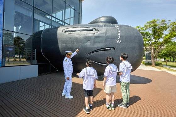 이해정(맨 왼쪽) 전 대령이 소중 학생기자단에게 돌고래급 잠수정의 함수 외부를 소개하고 있다.