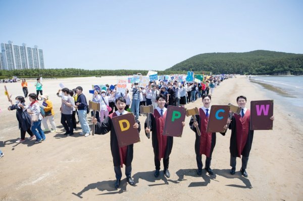 HWPL 부산경남서부지부가 세계평화선언문 발표 10주년을 맞아 지난 5월 25일 부산 다대포해수욕장에서 걷기대회를 개최한 가운데 회원들이 직접 제작한 DPCW 피켓을 들고 있는 모습. 사진제공ㅣ하늘문화세계평화광복 부산경남서부지부