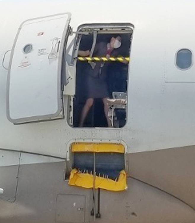 지난 26일 오후 제주공항에서 출발해 대구공항에 비상구 출입문이 열린 채 착륙한 아시아나항공기에서 한 승무원이 문에 안전바를 설치한 뒤 두 팔을 벌려 막고 있다. [사진출처 = 연합뉴스]