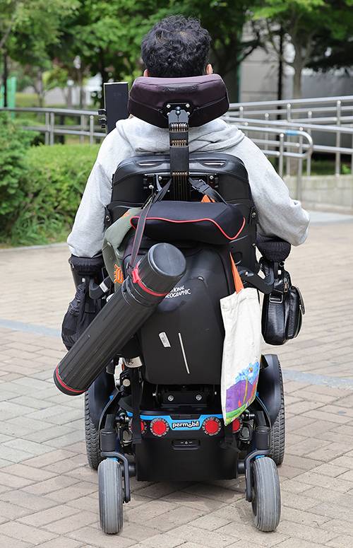 집을 나선 임 화가의 전동 휠체어 뒤에 화통이 걸려 있다.