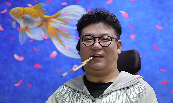 구필화가 임경식씨가 자신의 그림 앞에서 붓을 입에 물고 미소를 지어 보이고 있다.