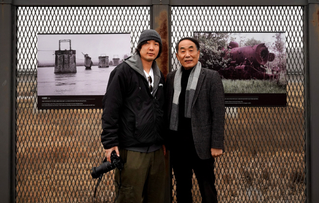 김녕만(오른쪽), 김호성 부자 작가가 분단을 주제로 한 사진 작품 앞에서 포즈를 취했다.  메타포32 제공