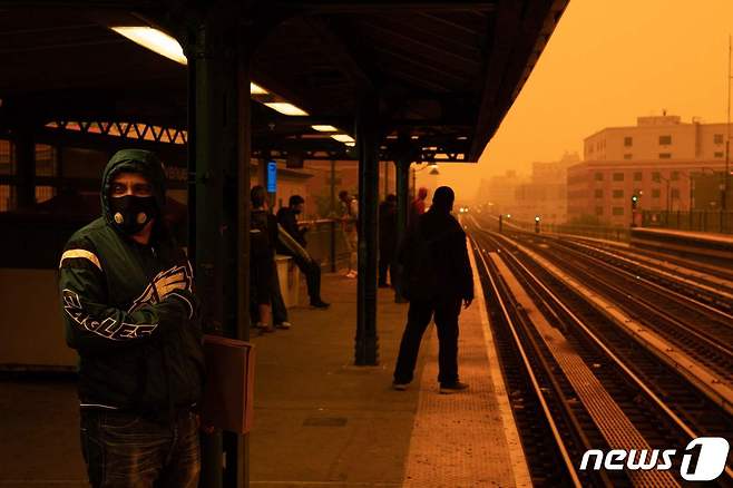 7일(현지시간) 캐나다 대형 산불 연기가 남하하면서 주황빛으로 물든 미국 뉴욕시 브롱스 상공. 지하철역에서 한 남성이 마스크를 쓰고 열차를 기다리고 있다. 2023.6.7 ⓒ AFP=뉴스1 ⓒ News1 정윤미 기자