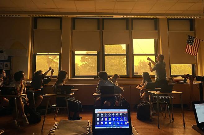 지난 7일 미 뉴욕주 펠햄의 한 고등학교 학생들이 수업하다 창밖으로 캐나다 산불 연기가 온통 하늘을 뒤덮은 일명 '오렌지 헤이즈' 현상을 내다보고 있다. 뉴욕 일대 학생들의 실외 활동이 전면 중단된 가운데, 실내에까지 연기가 파고들어와 대부분의 학교가 마스크를 쓰고 수업을 했다. /AP 연합뉴스