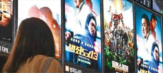 국내 4대 투자·영화배급사가 개봉한 영화가 올 들어 코로나19 이전의 3분의 1 수준으로 쪼그라들었다. 인건비 상승 등으로 제작비가 급등한 여파다. 서울의 한 영화관에서 관람객이 포스터를 바라보고 있다. 뉴스1