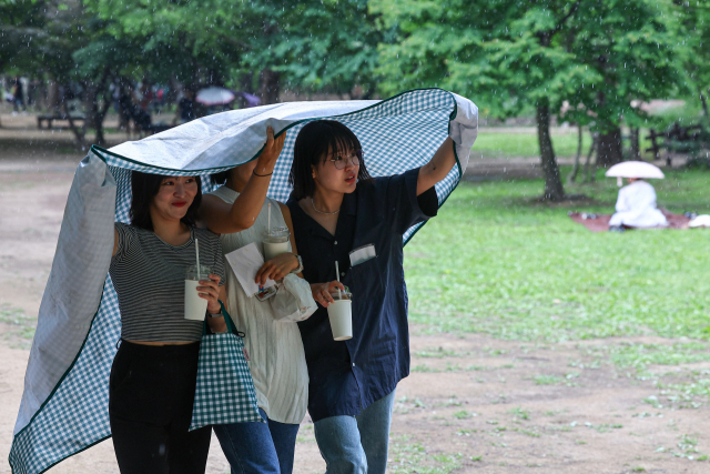 소나기가 내린 6일 오후 서울 성동구 서울숲에서 휴식하던 시민들이 갑자기 내린 비에 돗자리를 우산 삼아 쓰고 이동하고 있다. 연합뉴