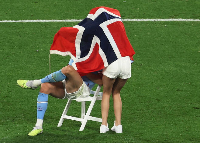 맨체스터 시티 엘링 홀란이 11일 터키 이스탄불에서 열린 유럽축구연맹 챔피언스리그에서 우승한 뒤 그라운드에 의자를 놓고 앉자  여자친구 아사벨 요한센이 노르웨이 국기로 감싸고 있다. 로이터연합뉴스